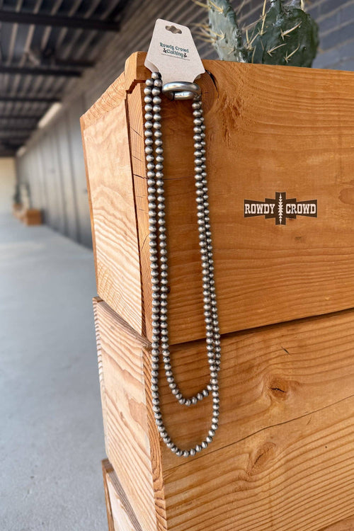 Wooden box with a necklace and 'Rowdy & Rund' branding in an indoor setting.