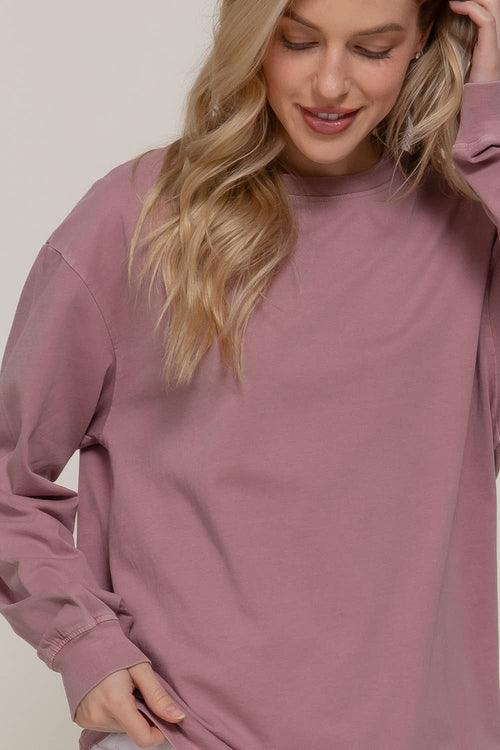A woman wearing a dusty rose long-sleeve crewneck sweatshirt, shown from the chest up against a plain light background.