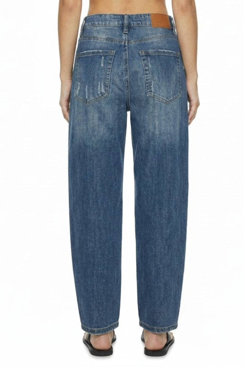 Rear view of a person wearing loose-fit blue denim jeans with a brown leather patch at the back waistband, shown against a plain white background.