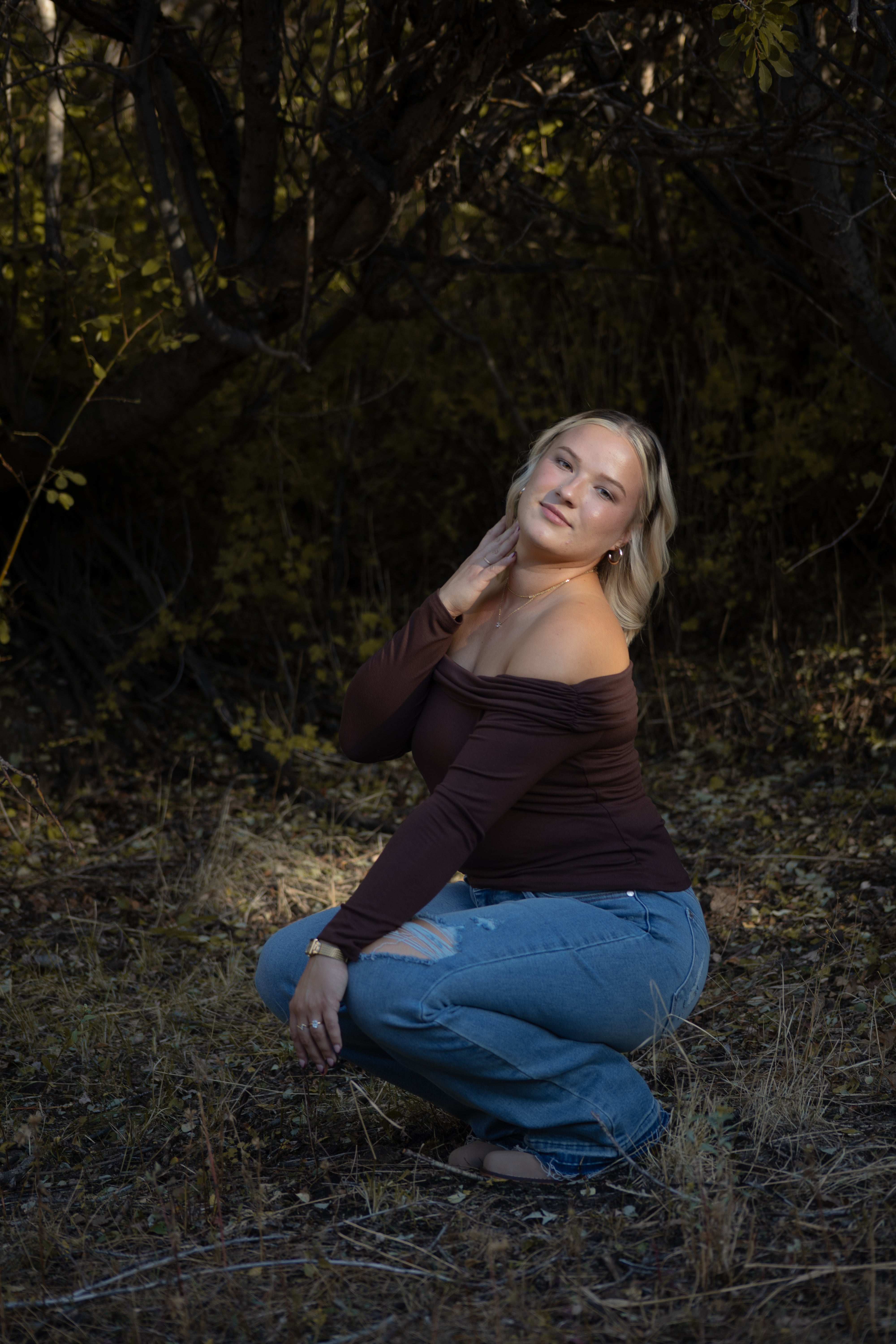 Woman sitting in a forested area with trees and dry grass in the background