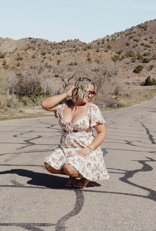 Woman in a horse dress squatting on a desert road with mountains in the background