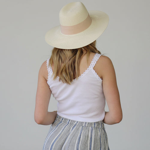 Person wearing a white sleeveless top and striped pants with a beige hat.