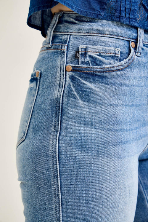 Close-up of a person wearing light blue denim jeans, showing the back pocket, button, rivets, and waistband area against a plain light background.