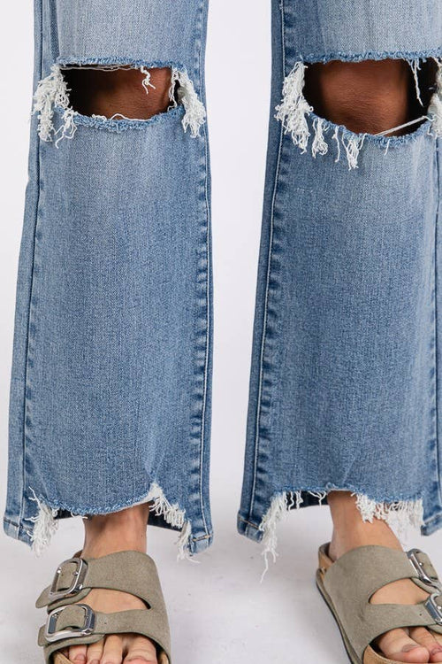 Ripped blue jeans worn with sandals on a white background