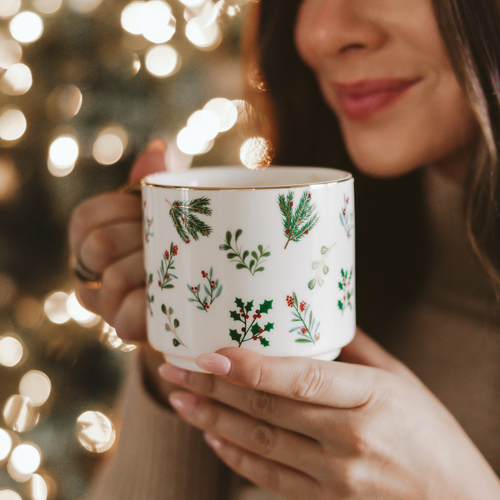 Person holding a mug with Christmas-themed design in front of a blurred festive background