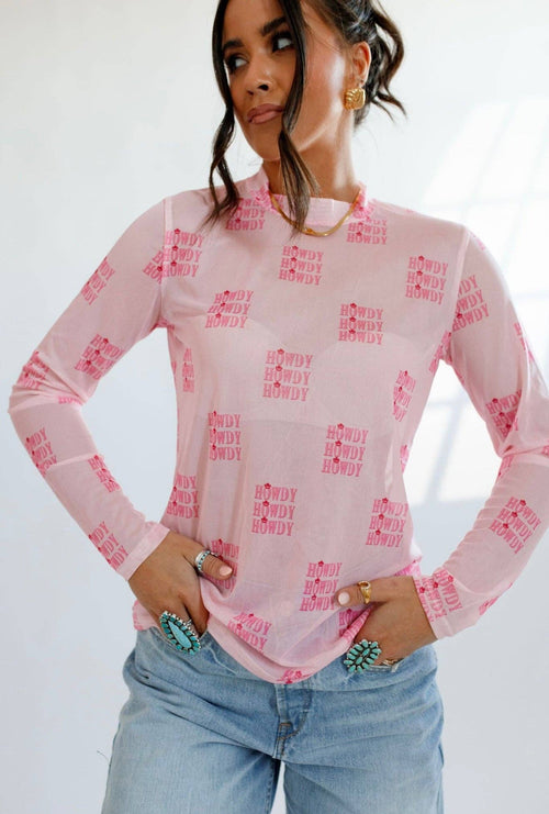 Woman wearing a pink long-sleeve top with text pattern and light blue jeans against a white background