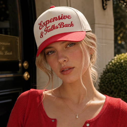 Woman wearing a red and white cap with text, standing outdoors.