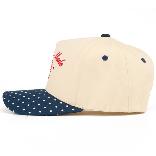 Two-tone cap with beige top and navy blue polka dot visor on a white background