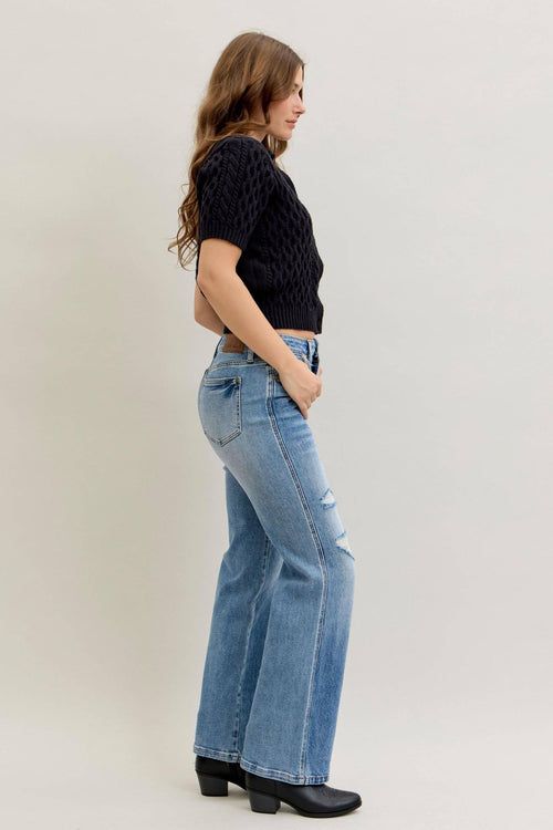 Woman wearing a black top and blue jeans against a plain background