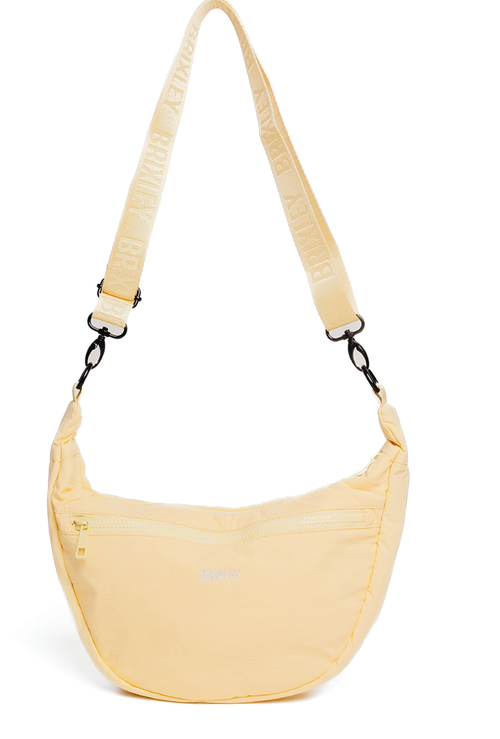 A pale yellow crescent-shaped nylon shoulder bag with a matching wide shoulder strap featuring white text, shown against a plain white background.