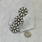 Decorative brooch with white stones on a marble surface with a coin for scale.
