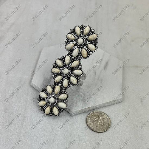 Decorative brooch with white stones on a marble surface with a coin for scale.
