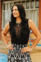 Woman wearing a black sleeveless top with pearl details and a patterned skirt outdoors.