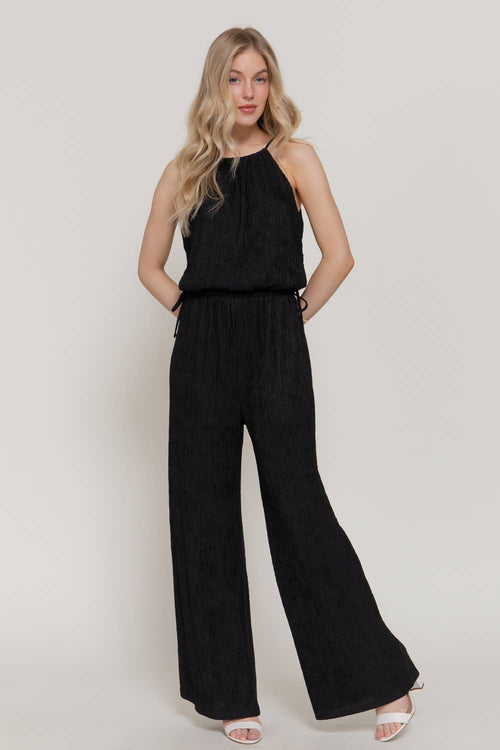 Woman wearing a black sleeveless top and wide-leg pants on a plain background