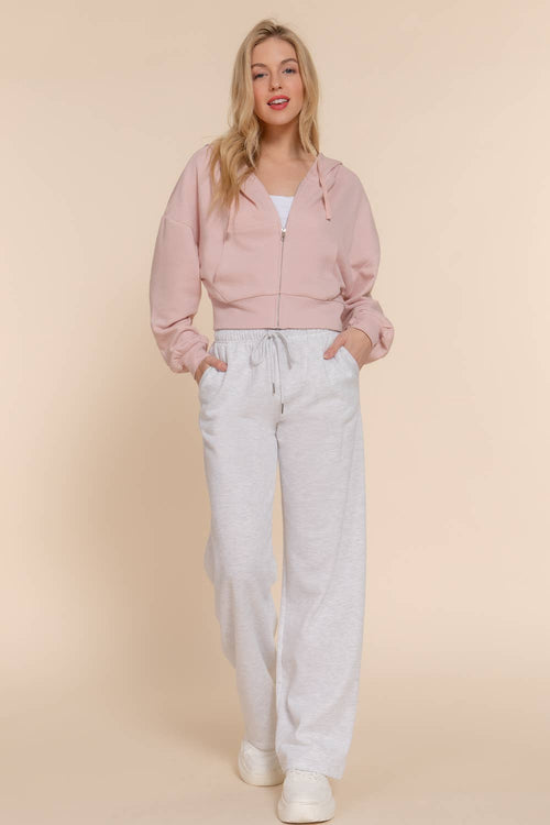Woman wearing a pink hoodie and light gray sweatpants on a beige background