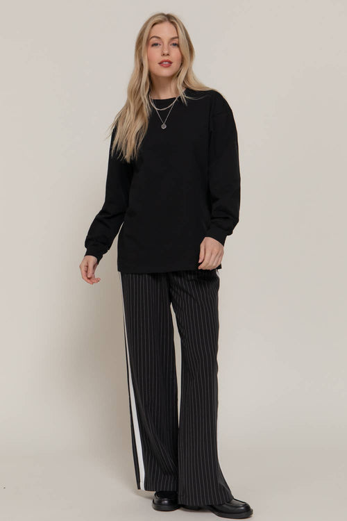 Woman wearing a black outfit with pinstriped pants against a plain background