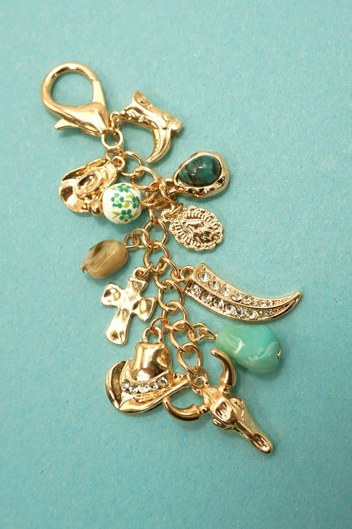 Gold charm keychain with various charms on a teal background
