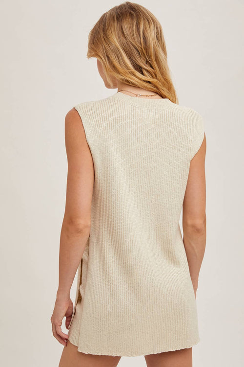 Woman wearing a beige sleeveless knitted dress against a plain background