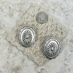 Silver concho-style earrings on a textured stone surface with a coin for scale.