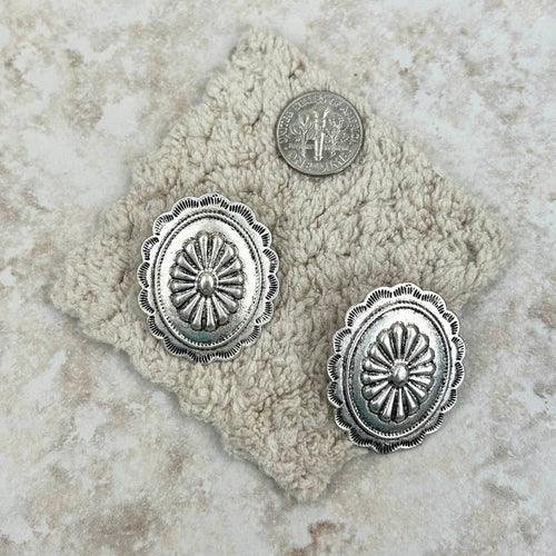 Silver concho-style earrings on a textured stone surface with a coin for scale.