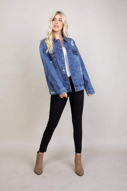 Woman wearing a denim jacket, black leggings, and brown boots on a plain background