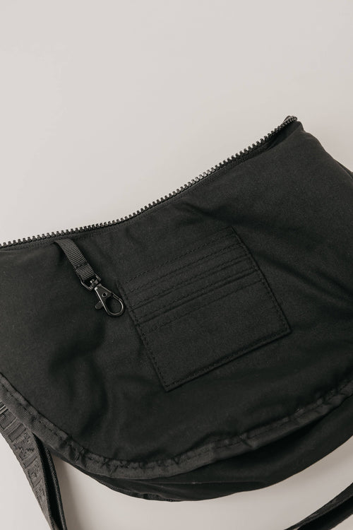 Close-up of a black fabric bag or pouch with a zipper, a small front pocket, and a strap, photographed on a light neutral background.