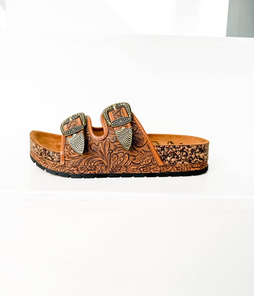 Brown leather sandal with decorative buckles on a white background