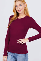 Woman wearing a burgundy sweater and blue jeans against a light gray background