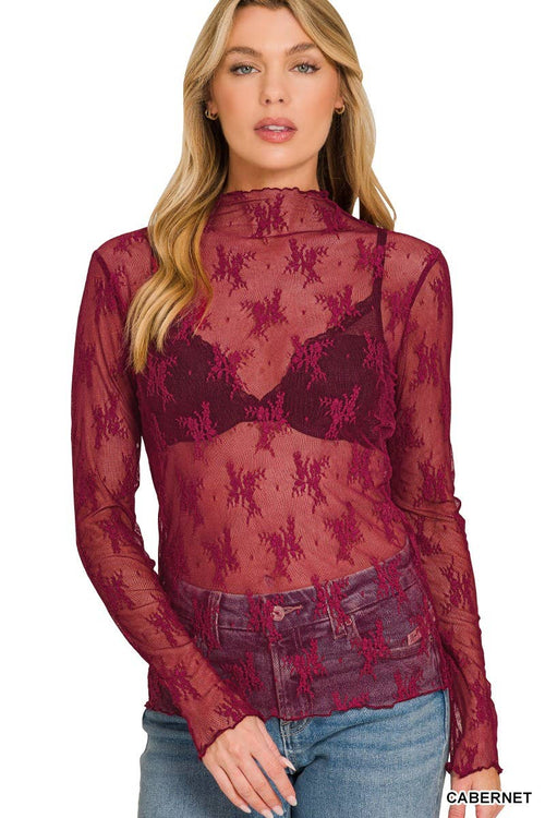 Woman wearing a sheer red lace top with long sleeves on a white background