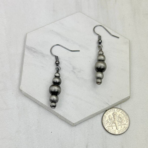 Pair of silver beaded earrings on a hexagonal marble tile with a coin for scale.