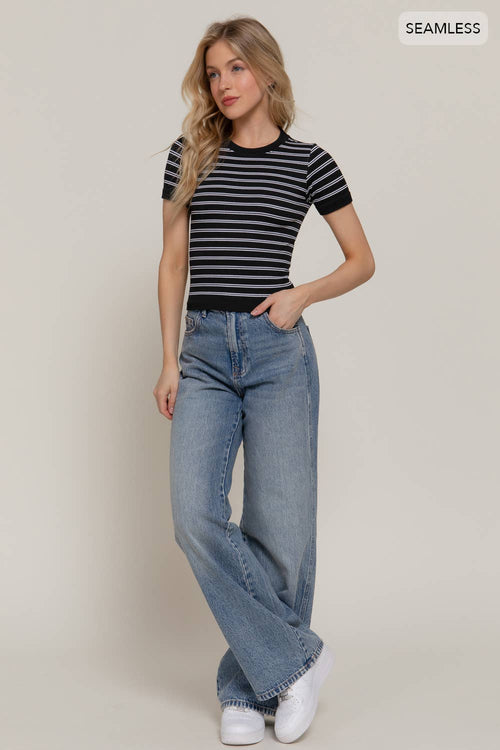 Woman wearing a striped black and white top and blue jeans on a plain background