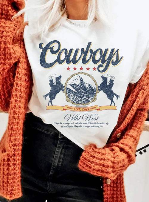 Person wearing a white hoodie with 'Cowboys Wild West' design, orange cardigan, and black pants.