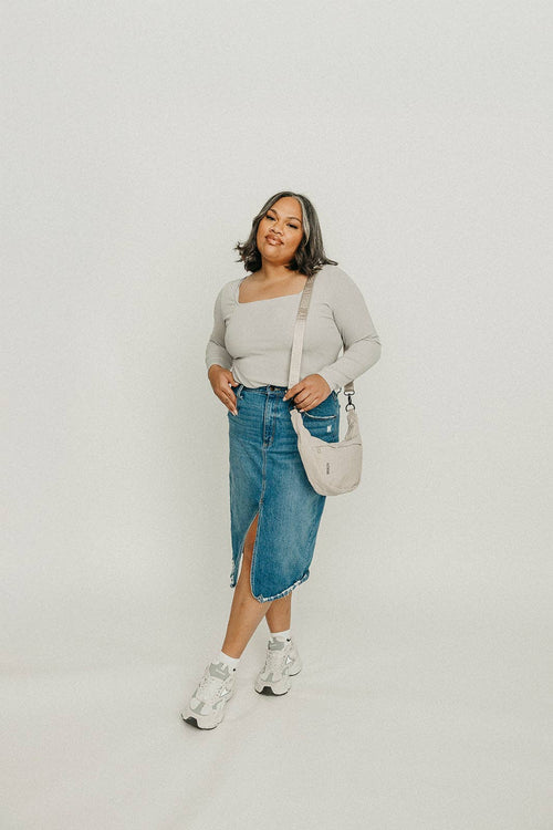 Woman wearing a light gray sweater, blue denim skirt, and white sneakers on a plain background