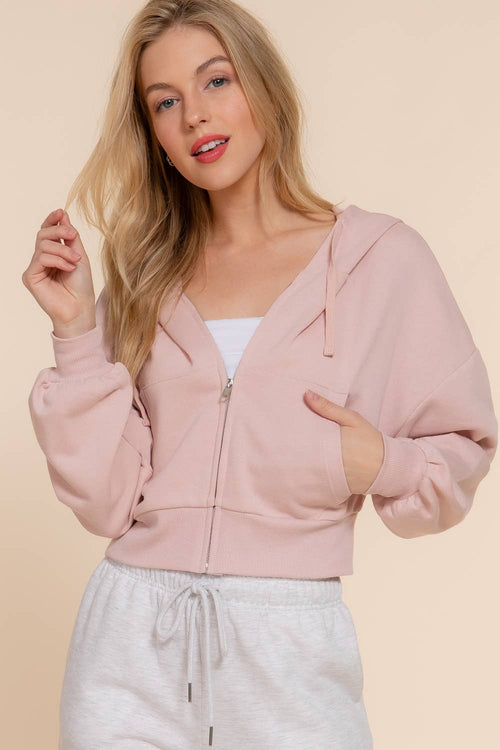 Woman wearing a pink zip-up hoodie and white pants on a beige background