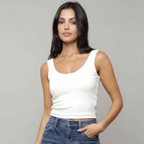 Woman wearing a white tank top and blue jeans with a neutral background
