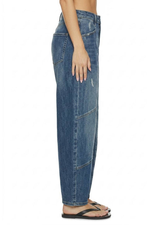 A side profile view of a person wearing wide-leg blue denim jeans and black flip-flop sandals against a plain white background.