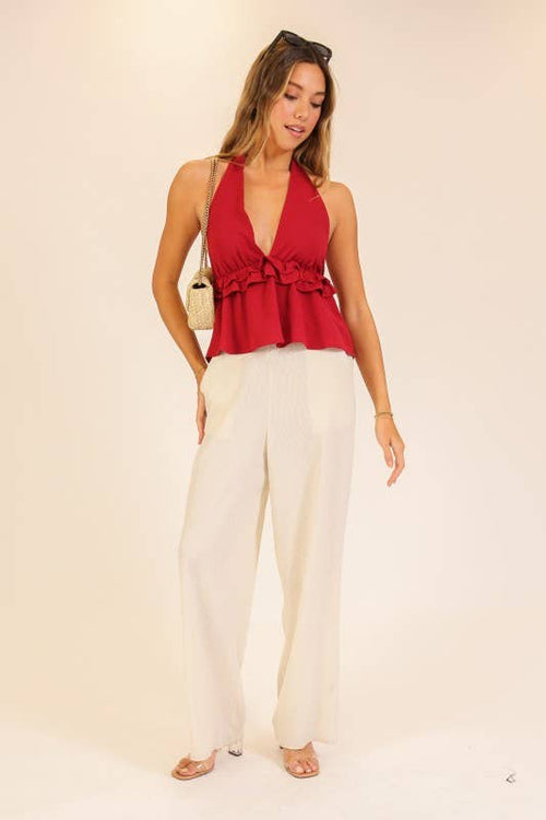 Woman wearing a red top and white pants on a beige background