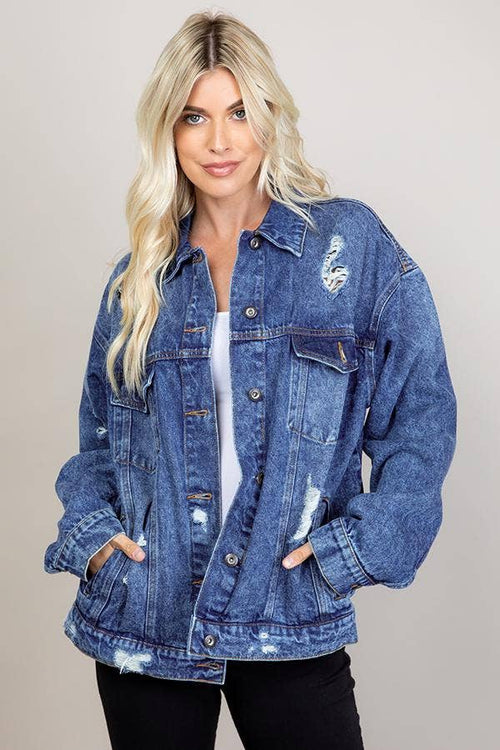 Woman wearing a blue denim jacket with patches on a plain background