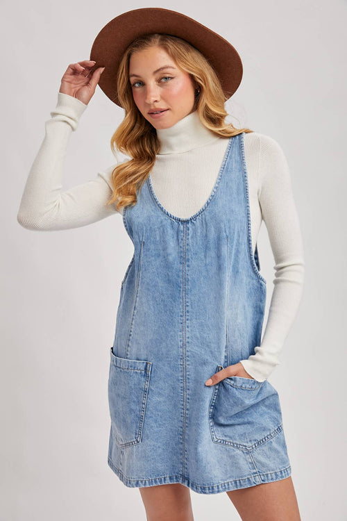 Woman wearing a denim dress and brown hat on a plain background
