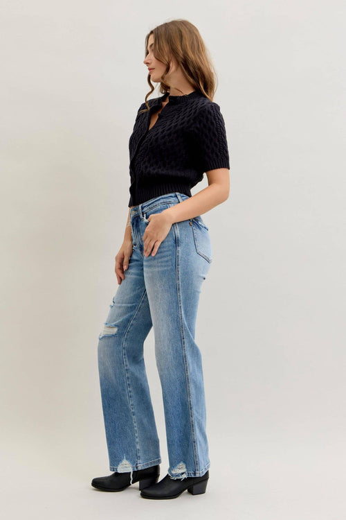Woman wearing a black top and blue jeans on a plain background