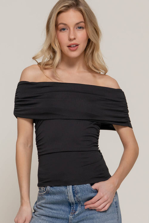 Woman wearing a black off-shoulder top and blue jeans against a plain background