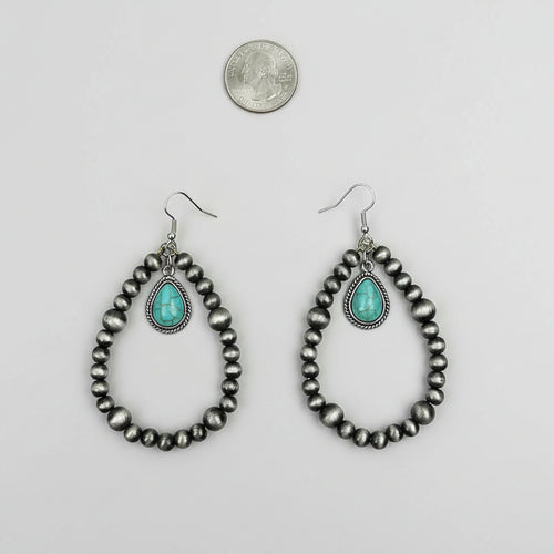 Pair of beaded earrings with turquoise stones on a white surface, next to a quarter for scale.