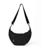 A black crescent-shaped shoulder bag with a white polka dot pattern and an adjustable black strap, shown on a plain white background.