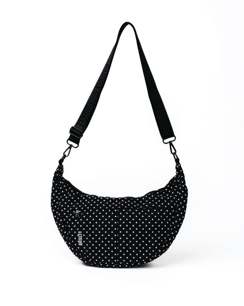 A black crescent-shaped shoulder bag with a white polka dot pattern and an adjustable black strap, shown on a plain white background.