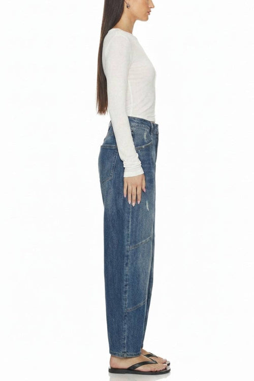 A side-profile view of a model wearing high-waisted, wide-leg blue denim jeans, a white long-sleeve top, and black flip-flop sandals against a plain white background.