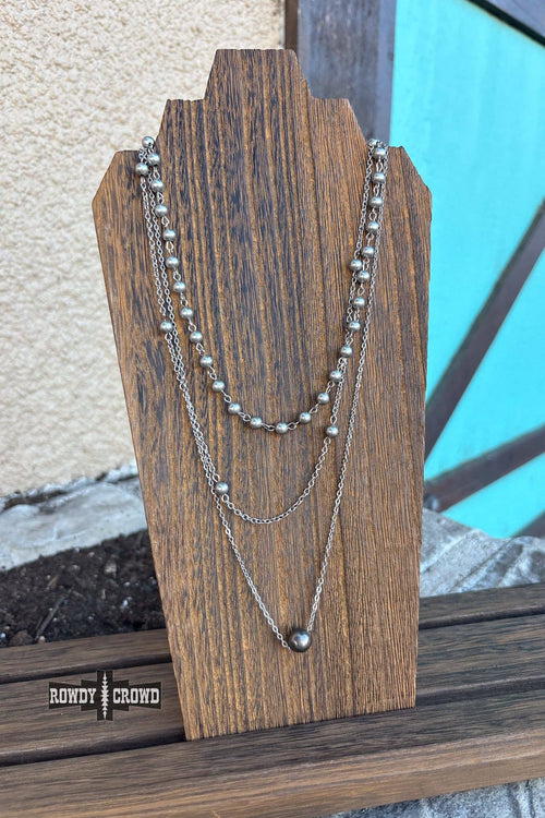 Three silver necklaces on a wooden stand with a blurred background