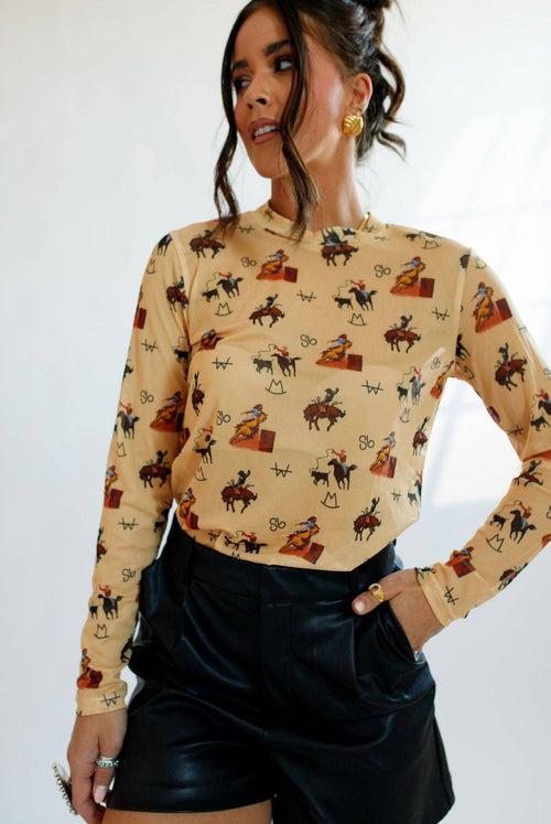 Woman wearing a beige long-sleeve top with cowboy print and black leather shorts on a white background