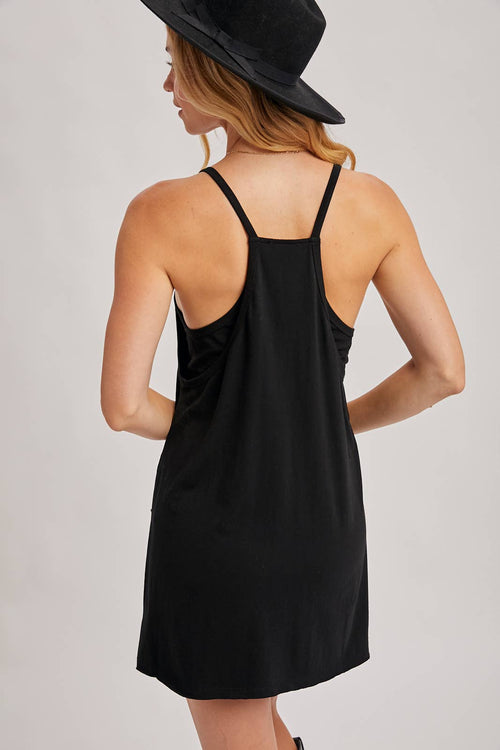 Woman wearing a black slip dress and black hat on a plain background