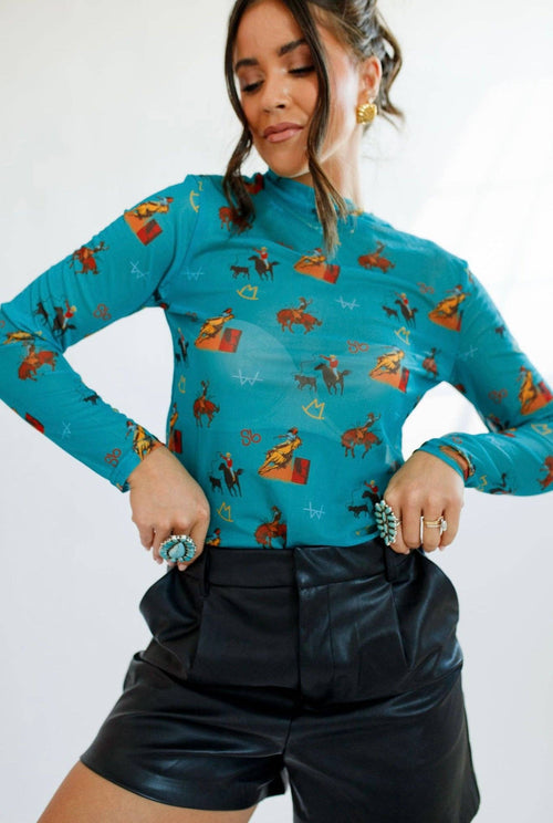 Woman wearing a turquoise long-sleeve top with pattern and black shorts on a white background