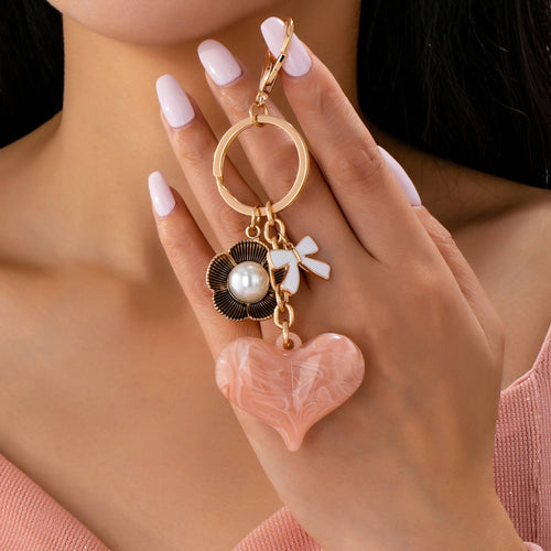 Hand holding a decorative keychain with a heart charm, pearl, and bow.